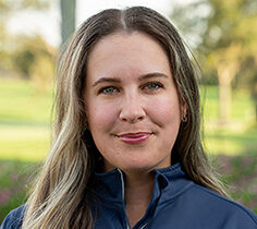 Head and shoulders photograph of a smiling Katie Jackson, Program Director and Level 4 Coach of First Tee – Sarasota/Manatee standing proudly in front of a golf course.