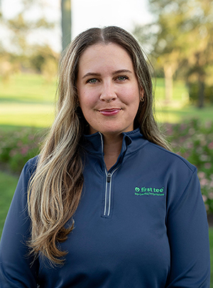 Head and shoulders photograph of a smiling Katie Jackson, Program Director and Level 4 Coach of First Tee – Sarasota/Manatee standing proudly in front of a golf course.