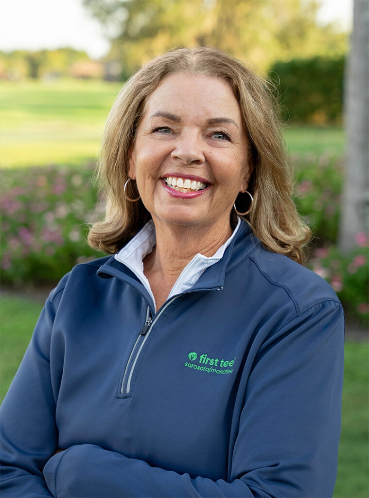 Head and shoulders photograph of a smiling Lexi McKenney, Director of Chapter Relations and Level 1 Coach of First Tee – Sarasota/Manatee standing proudly in front of a golf course.