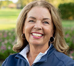 Head and shoulders photograph of a smiling Lexi McKenney, Director of Chapter Relations and Level 1 Coach of First Tee – Sarasota/Manatee standing proudly in front of a golf course.