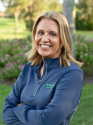 Head and shoulders photograph of a smiling Lisa Krouse, Esq., SCP, SPHR, Chief Executive Officer of First Tee – Sarasota/Manatee standing proudly in front of a golf course.
