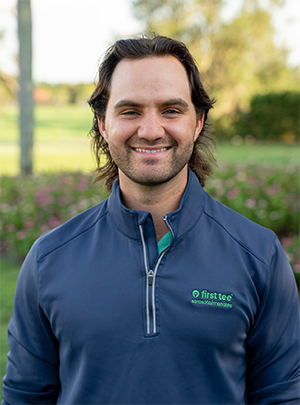 Head and shoulders photograph of a smiling Noah Cronin, Program Coordinator of Manatee County, Level 2 Coach and TPI Certified Level 1 of First Tee – Sarasota/Manatee standing proudly in front of a golf course.